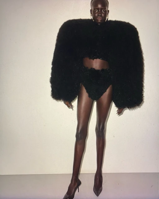 A striking fashion image featuring a black female model wearing avant-garde black high-fashion attire and high heels against a white backdrop.