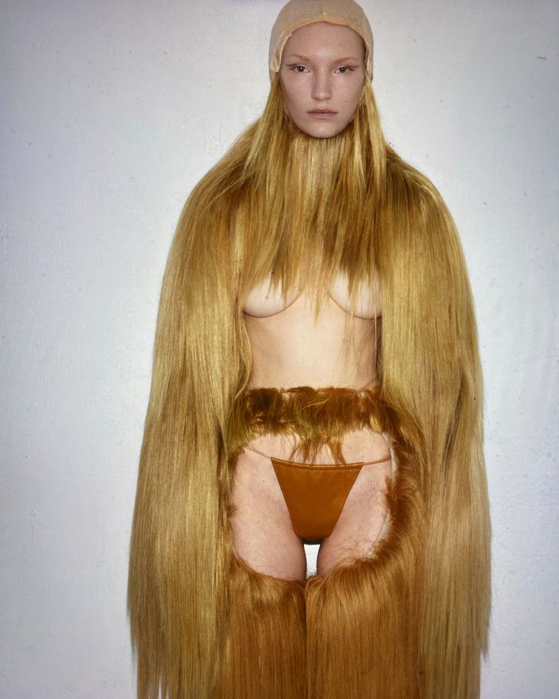 Model with long blonde hair extensions and tan bodysuit posing in a white photo studio. Fashion and beauty concept.