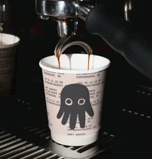 Espresso machine dispensing coffee into a branded paper cup featuring an illustration on a dark background