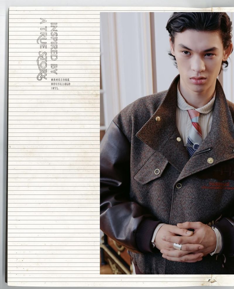 Portrait of a young adult wearing a brown jacket, tie, and ring, shot indoors with a magazine cover featuring lined paper on the left.