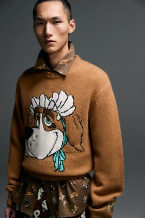 Stylish portrait of an Asian man in a brown sweater featuring an animated dog design. He is also wearing a patterned shirt underneath.