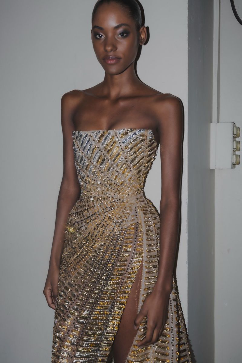 Portrait of an African American woman wearing a gold sequin gown with a slit in a studio with a neutral background, beauty shot.