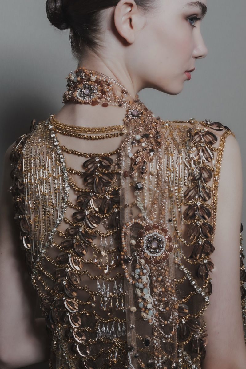 Adult woman in an elaborate gold beaded gown and choker, seen from the back in a studio setting. Beauty and fashion shot.