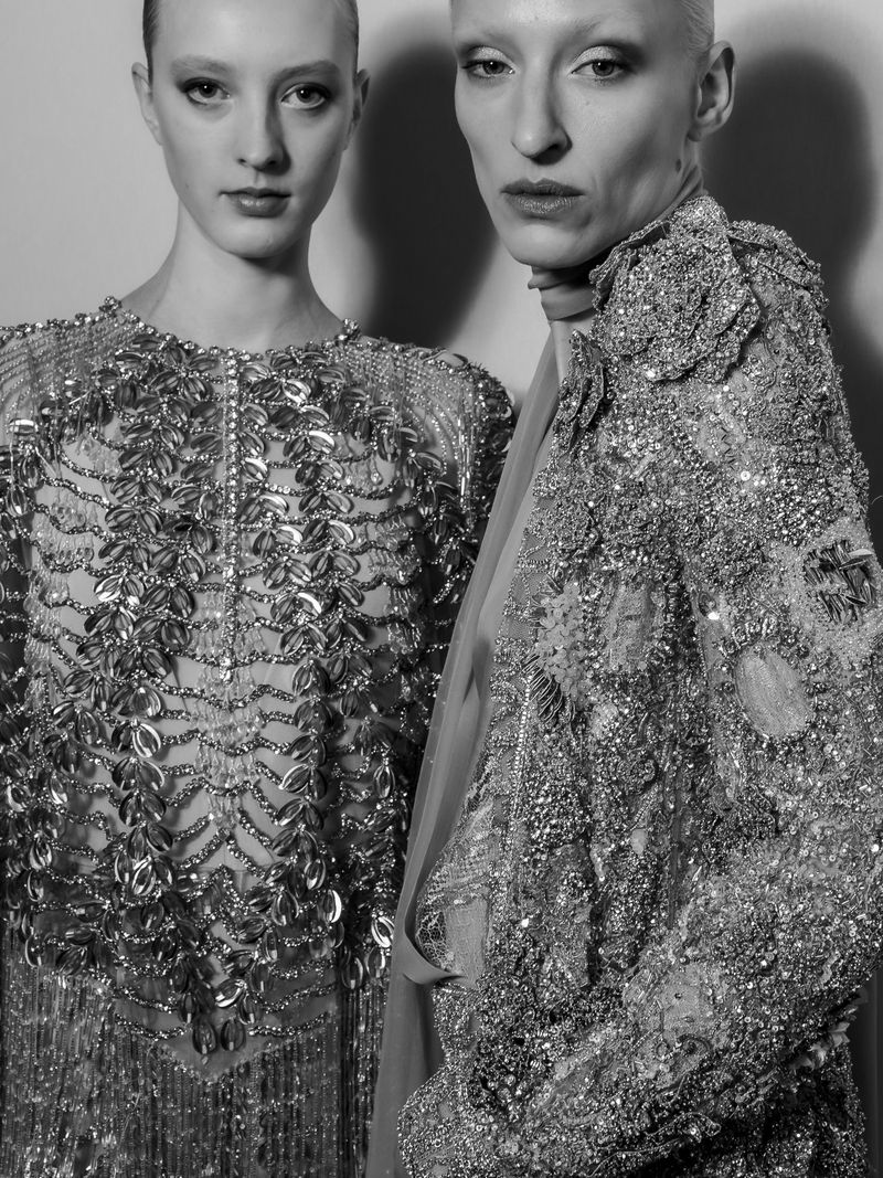 Two women in beaded gowns pose in a close-up studio shot, showcasing intricate details and monochrome elegance in a fashion editorial.