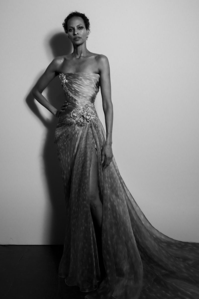 Black and white portrait of a woman wearing a formal gown with floral accents, standing in a studio setting.