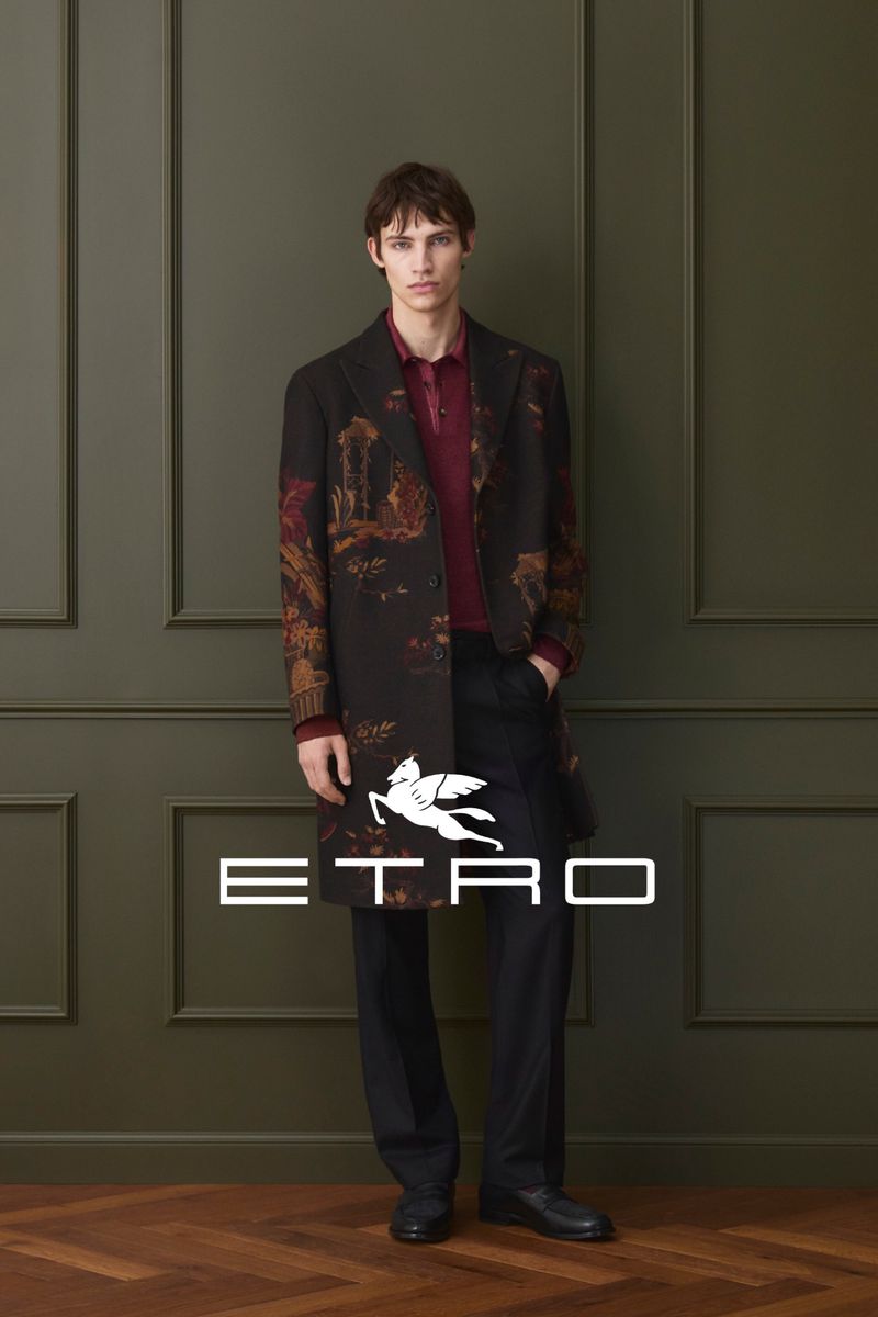 A young adult male stands indoors wearing a printed overcoat, burgundy polo shirt, and black pants, with the Etro logo displayed in the foreground.
