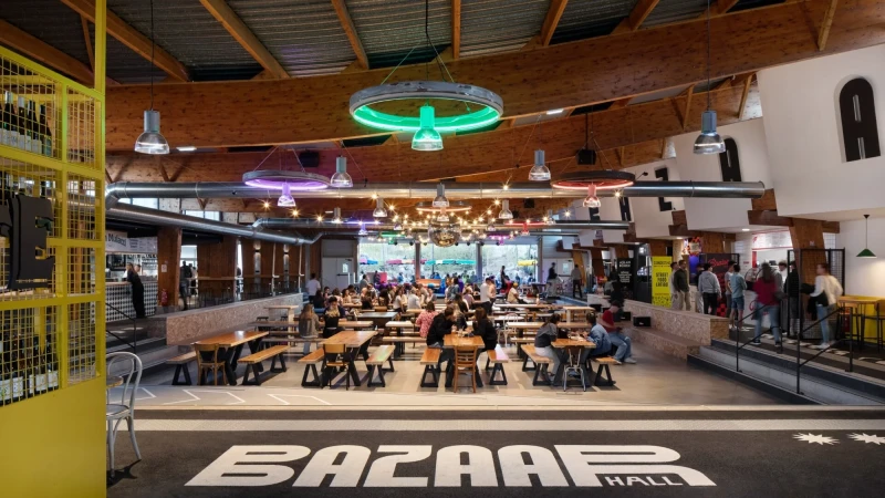 Interior view of Bazaar Hall with numerous people seated at tables, illuminated by hanging lights, creating a lively and inviting atmosphere.