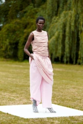 Model Hakima Athuai wearing a pink sleeveless top and trousers standing on a white platform outdoors for Odeeh Spring 2026