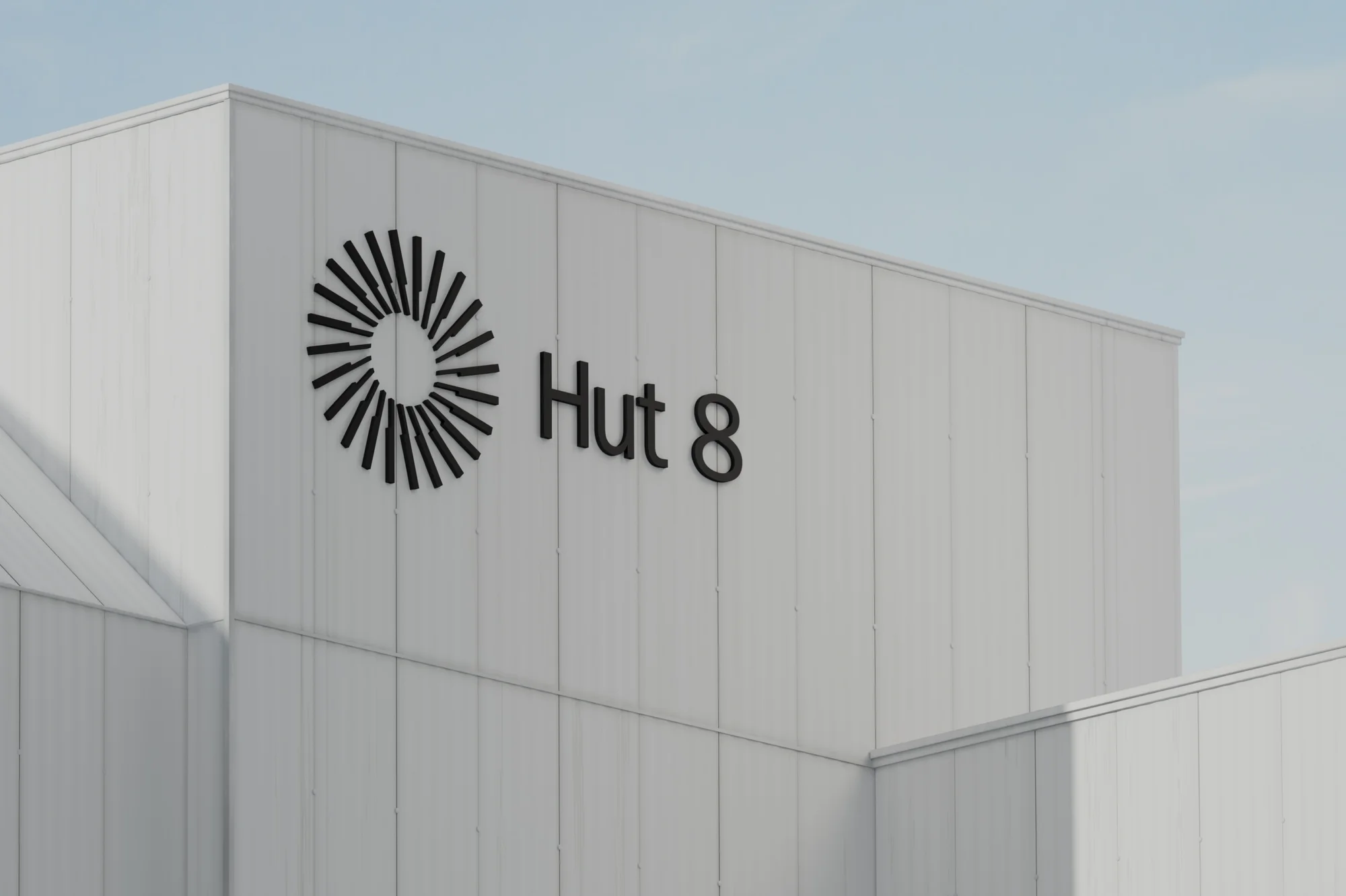 Exterior shot of a modern white building with the black 'Hut 8' logo and circular design, against a clear, light blue sky.