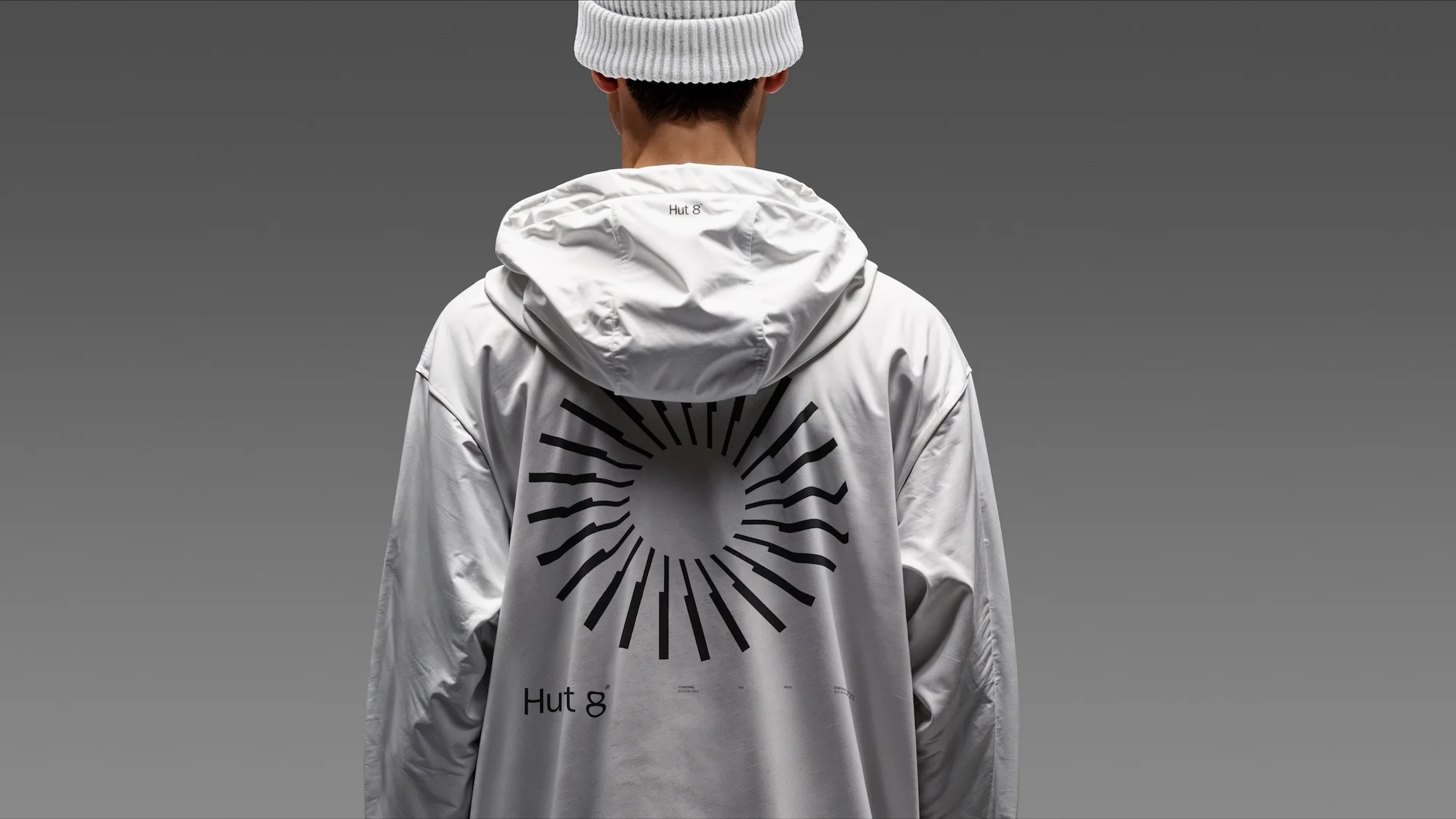 Back view of a person wearing a white hooded jacket with a geometric design, paired with a matching hat against a grey background.