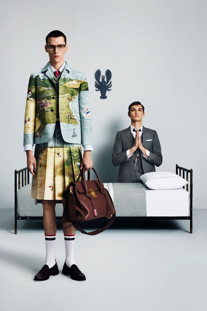 Two men in a studio setting; one wearing a landscape blazer and kilt, the other a suit praying over a bed with a lobster on the wall.