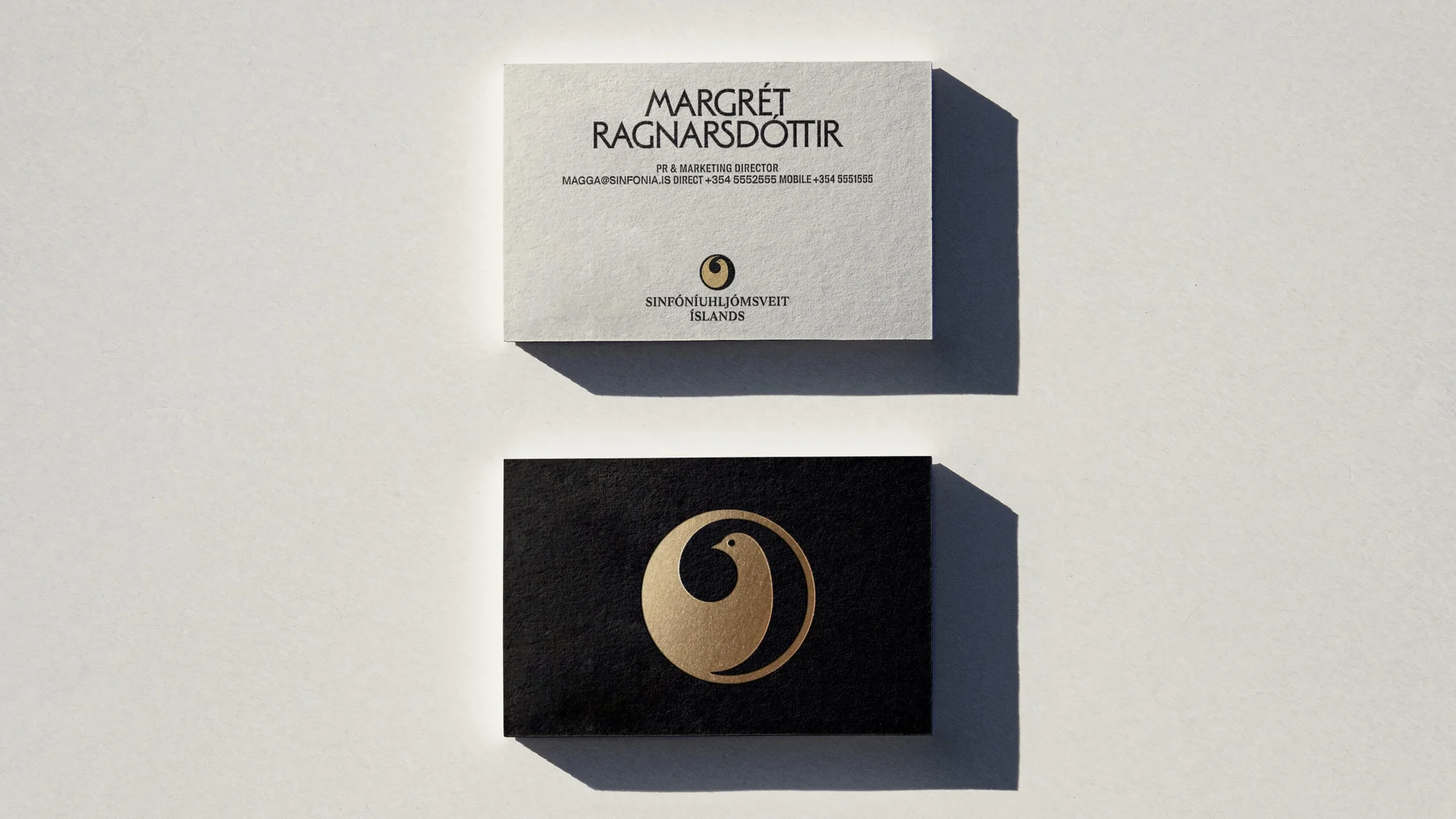 Two business cards, one white with text and a small gold logo, and one black with a large gold logo, on white background.