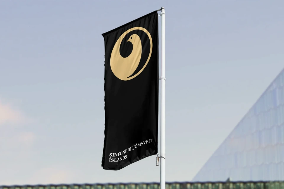 Flag of the Iceland Symphony Orchestra on a white pole. The flag is black with a gold logo and white text at the bottom.