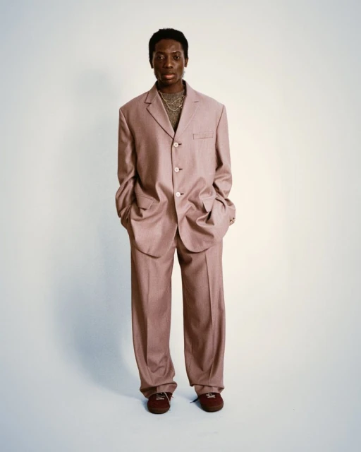 Full body portrait of an African American man in a blush pink suit with matching trousers posing against a white backdrop.