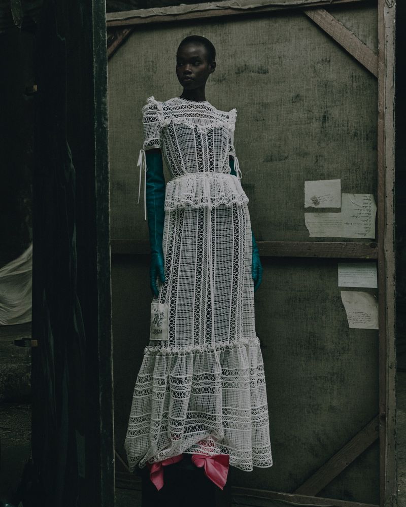 Fashionable Black woman poses in a sheer white lace dress with turquoise gloves, in a grungy studio with peeling paint and wood.