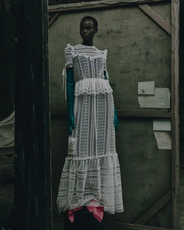 Fashionable Black woman poses in a sheer white lace dress with turquoise gloves, in a grungy studio with peeling paint and wood.