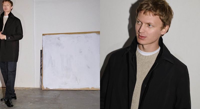 Man in a black coat stands in front of a white painting in a minimalist space, creating a fashion editorial look. 