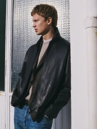 Model Jonas Glöer in a black leather jacket and blue jeans leaning against a building exterior for Massimo Dutti Perspectives