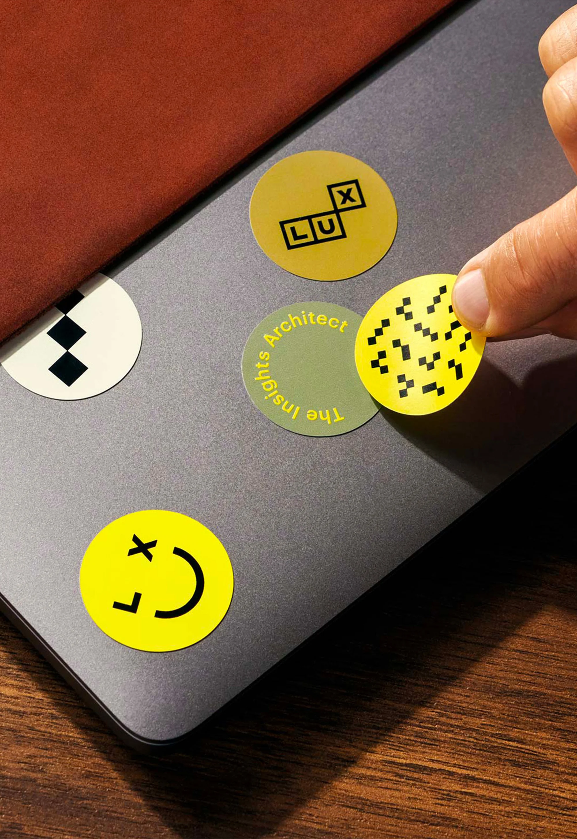Laptop decorated with graphic circular stickers, featuring hand placing a sticker with a pixelated design on the surface.