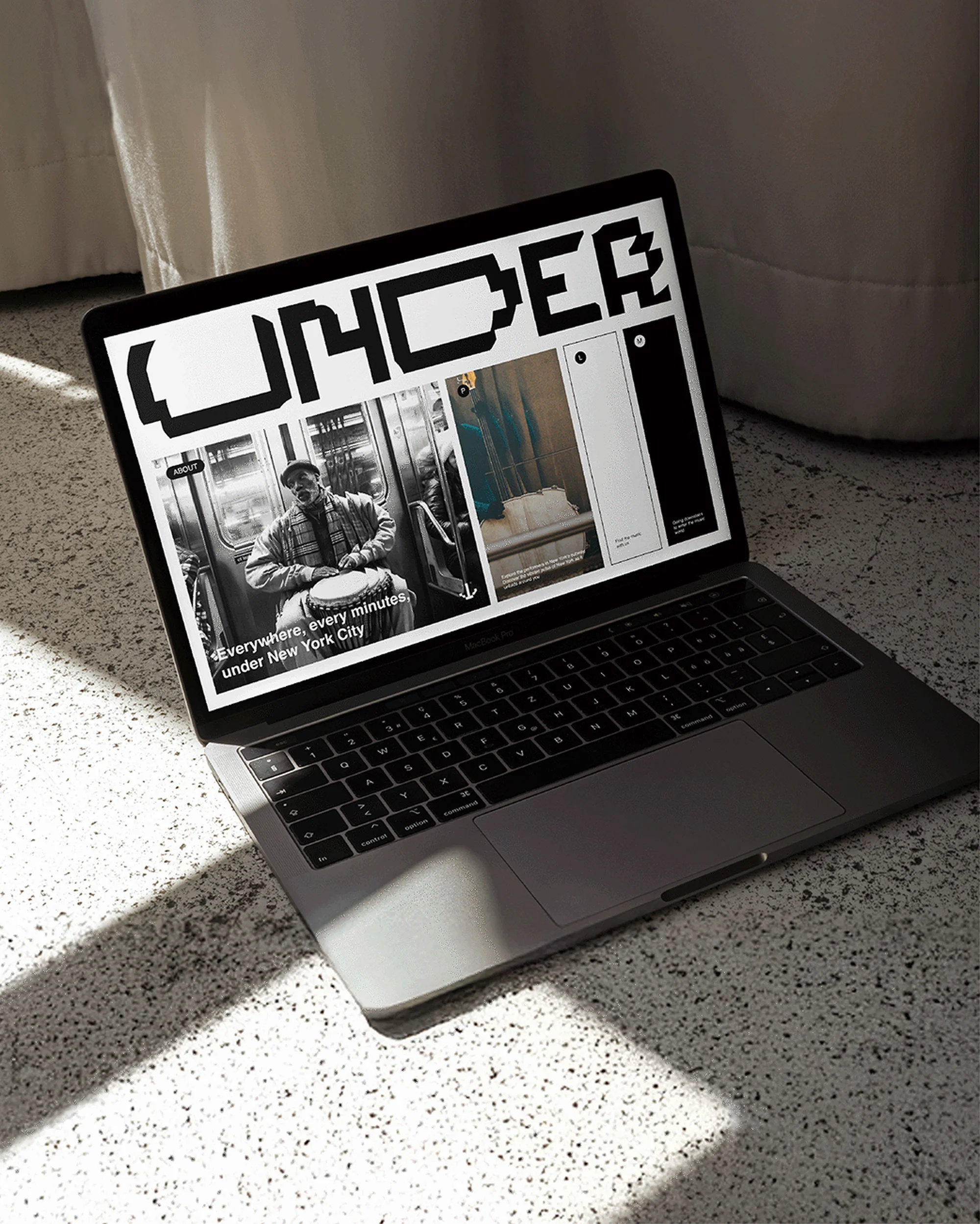 Laptop displaying 'UNDER' website on a speckled surface with light and shadow interplay, focusing on design and technology elements.