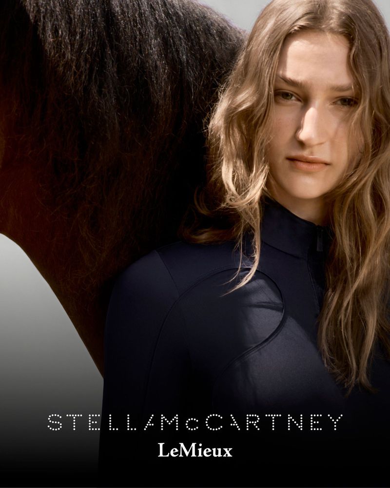 A woman with wavy blonde hair poses next to a dark brown horse for a fashion advertisement with Stella McCartney and LeMieux logos.