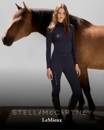 Model standing next to a brown horse in navy equestrian wear against a neutral grey studio background with brand text.