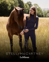 Model standing in a golden meadow next to a brown horse, wearing dark equestrian athletic wear for Stella McCartney x LeMieux.