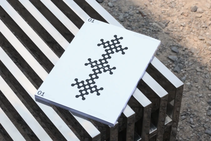 An abstract-patterned book cover on a contemporary bench with a chrome-finished metal frame, set against a neutral outdoor backdrop.