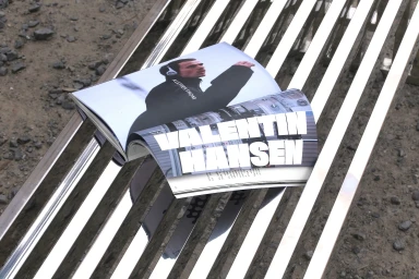 Open magazine displaying editorial imagery resting on a reflective slatted metallic bench outdoors