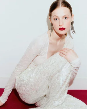 Model in white textured top and trousers wearing long fringe earrings against a plain white background