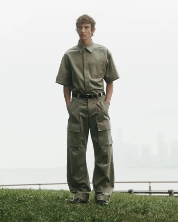 Model wearing an olive green short sleeve button-down shirt and matching utility cargo trousers standing outdoors.