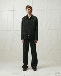 Model wearing a black button-up jacket and matching trousers against a white backdrop.