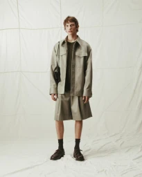 Model wearing a grey buttoned jacket and matching shorts against a white textured backdrop