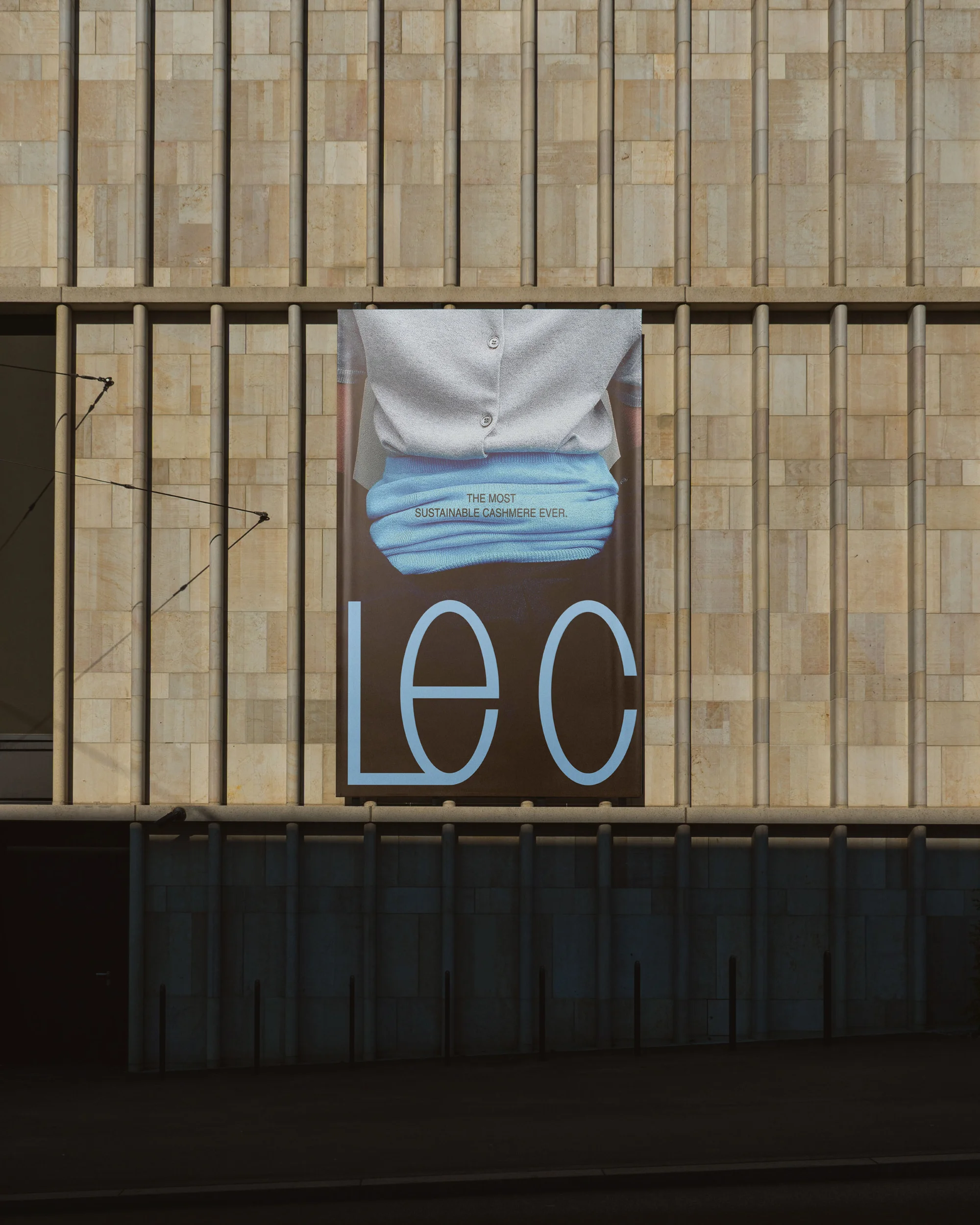 Fashion advertisement poster on building facade featuring a folded sustainable garment, with brand logo LEC prominently displayed.