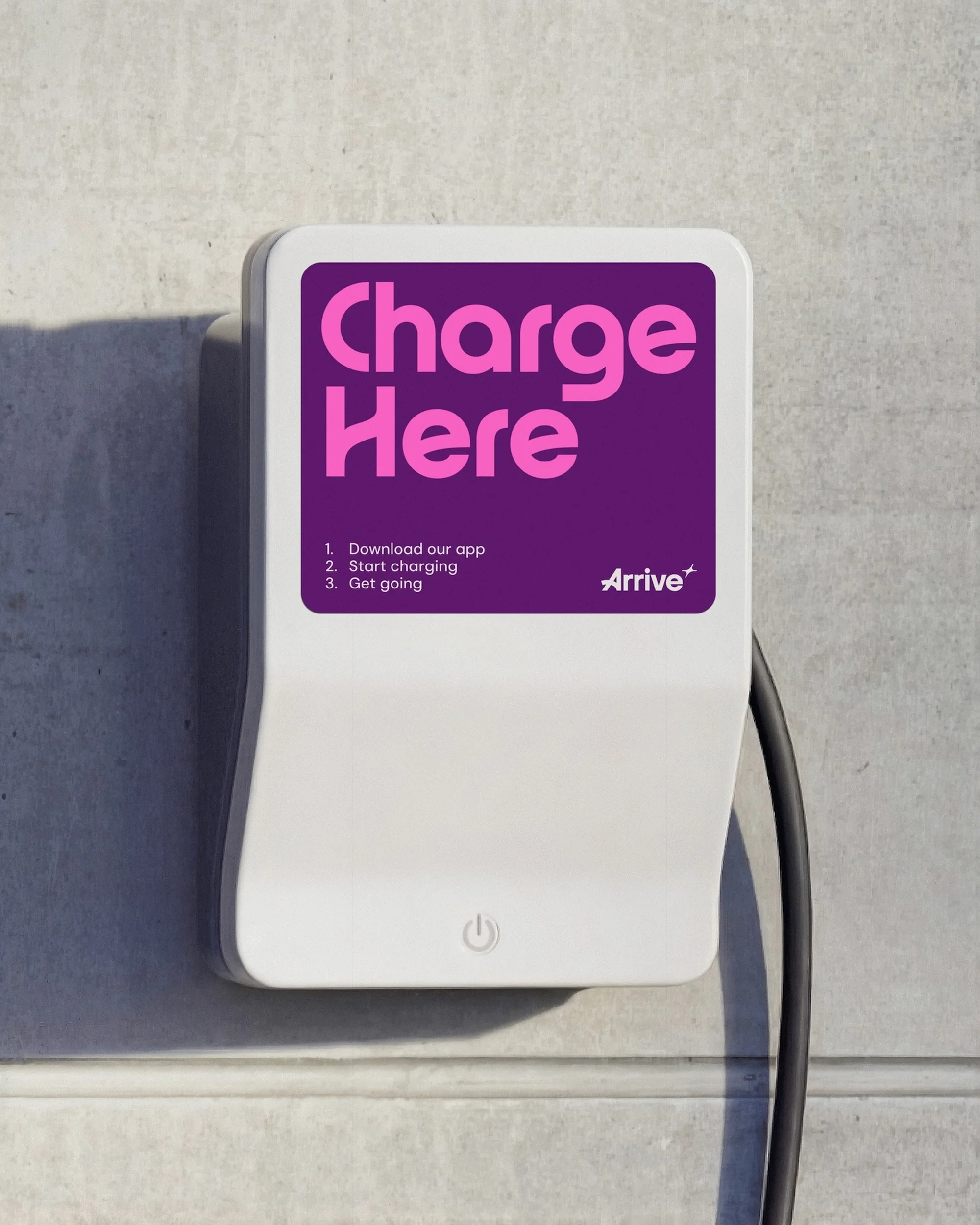 Electric vehicle charger mounted on a wall with the words 'Charge Here' in pink lettering on a purple background.