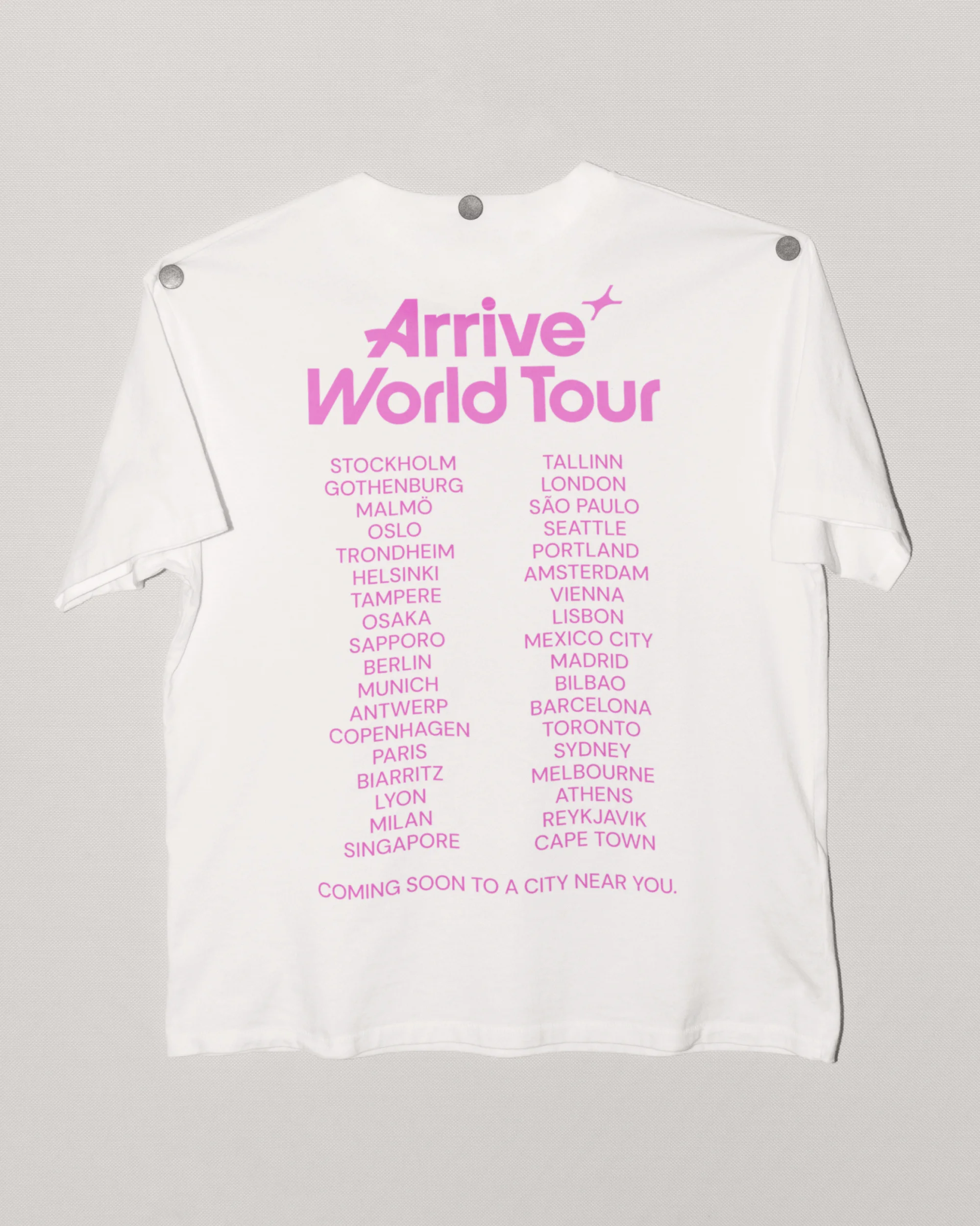 White t-shirt with 'Arrive World Tour' in pink text, listing cities like Stockholm, London, Mexico City, and Cape Town in pink.