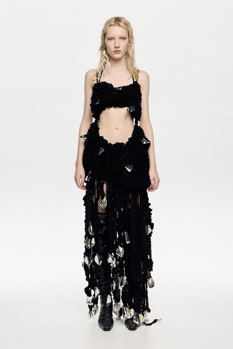 Full-length shot of a fair-skinned adult female fashion model in a black two-piece outfit with fringe and crystal accents in a photo studio.