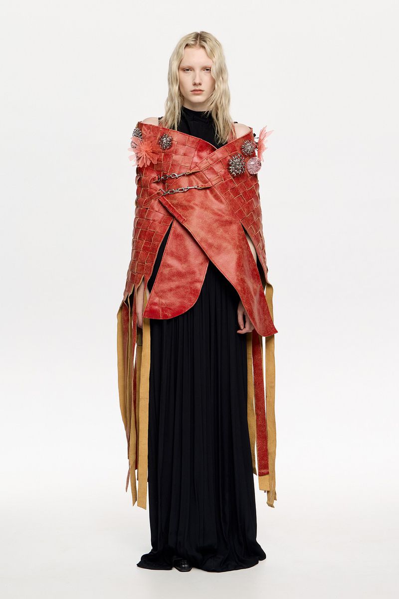 Woman in avant-garde red coat and black dress against white backdrop. Dramatic fashion portrait showcasing unique design elements.