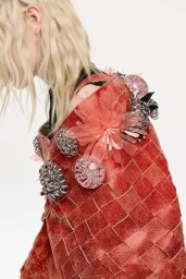Close-up portrait of model Ivy Stewart in a red woven upcycled garment adorned with translucent floral appliqués and metallic embellishments.