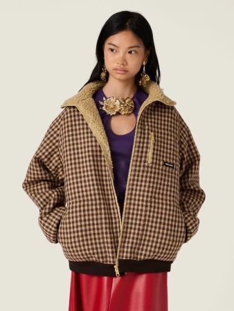 Fashionable Asian woman in a brown and beige checkered jacket with a faux fur collar, posing in a studio with neutral lighting.