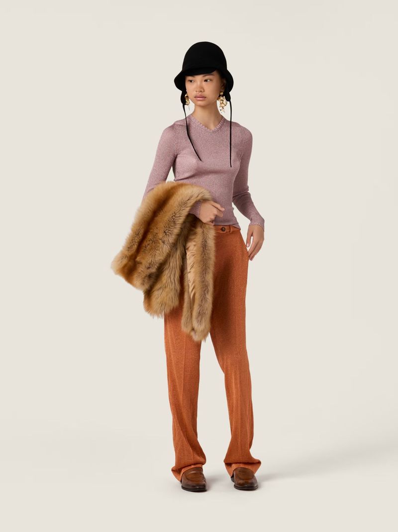 Full-length studio shot of an Asian woman wearing a pink top, orange slacks, black hat, brown shoes, and holding a fur stole over her shoulder.