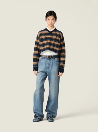 An Asian woman wearing a cropped sweater, button-down shirt, wide-leg jeans, and chunky shoes stands in a brightly lit neutral studio.
