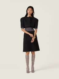 Model Yue Gu wearing a dark textured cropped jacket and skirt set against a white studio background for Miu Miu.