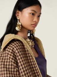 Close-up portrait of model Yue Gu wearing a brown houndstooth jacket and large gold floral earrings for Miu Miu.