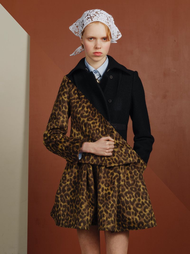 Fashion editorial portrait of a young woman wearing a leopard print skirt and coat with black jacket and white lace headscarf.