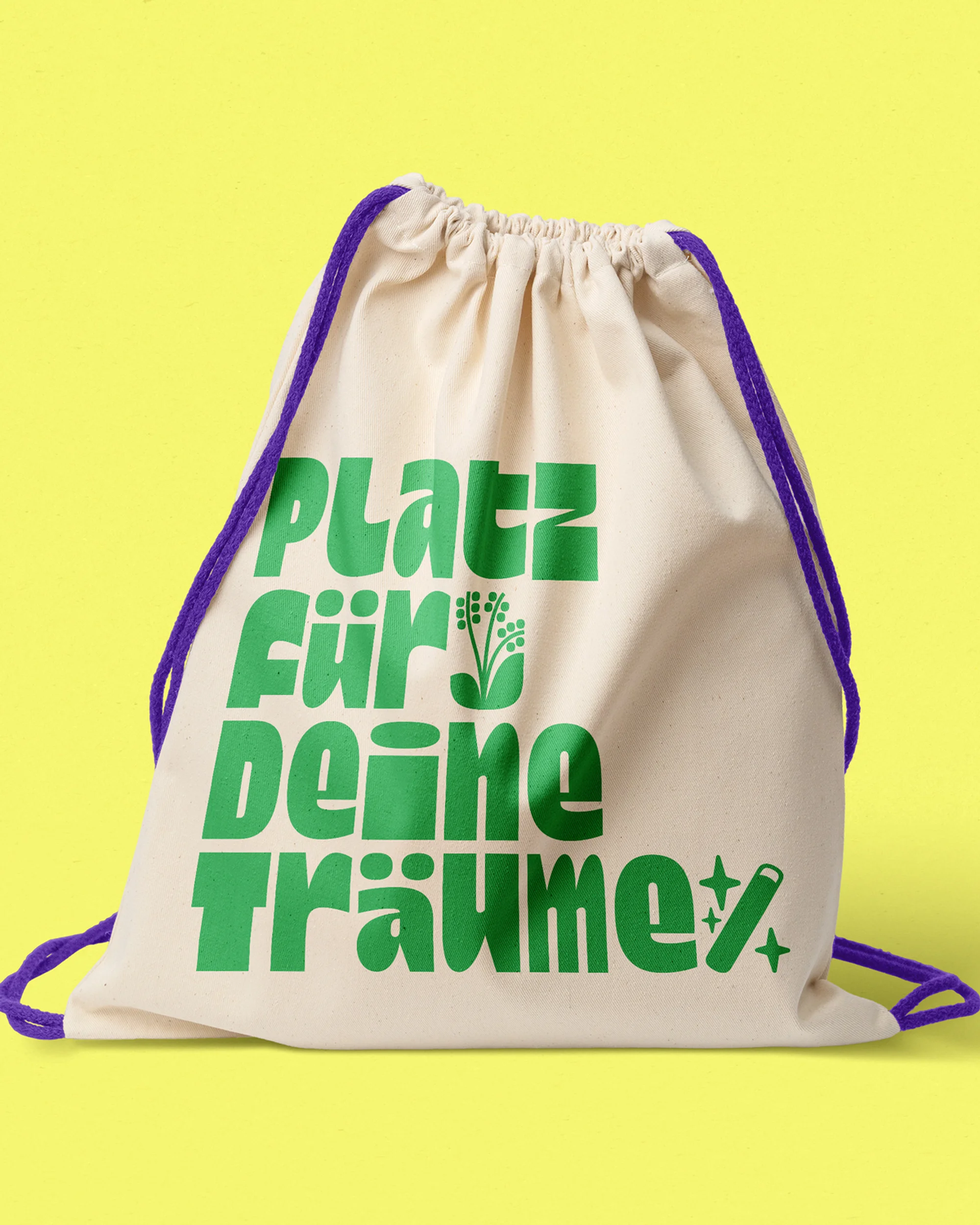 Beige drawstring bag with green text 'Platz für Deine Traüme' and purple drawstrings against a vibrant yellow background.