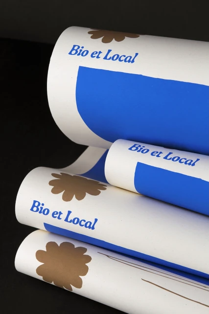 Stack of white rolls of paper with brown floral design and text "Bio et Local" in blue ink on a black background, close-up.