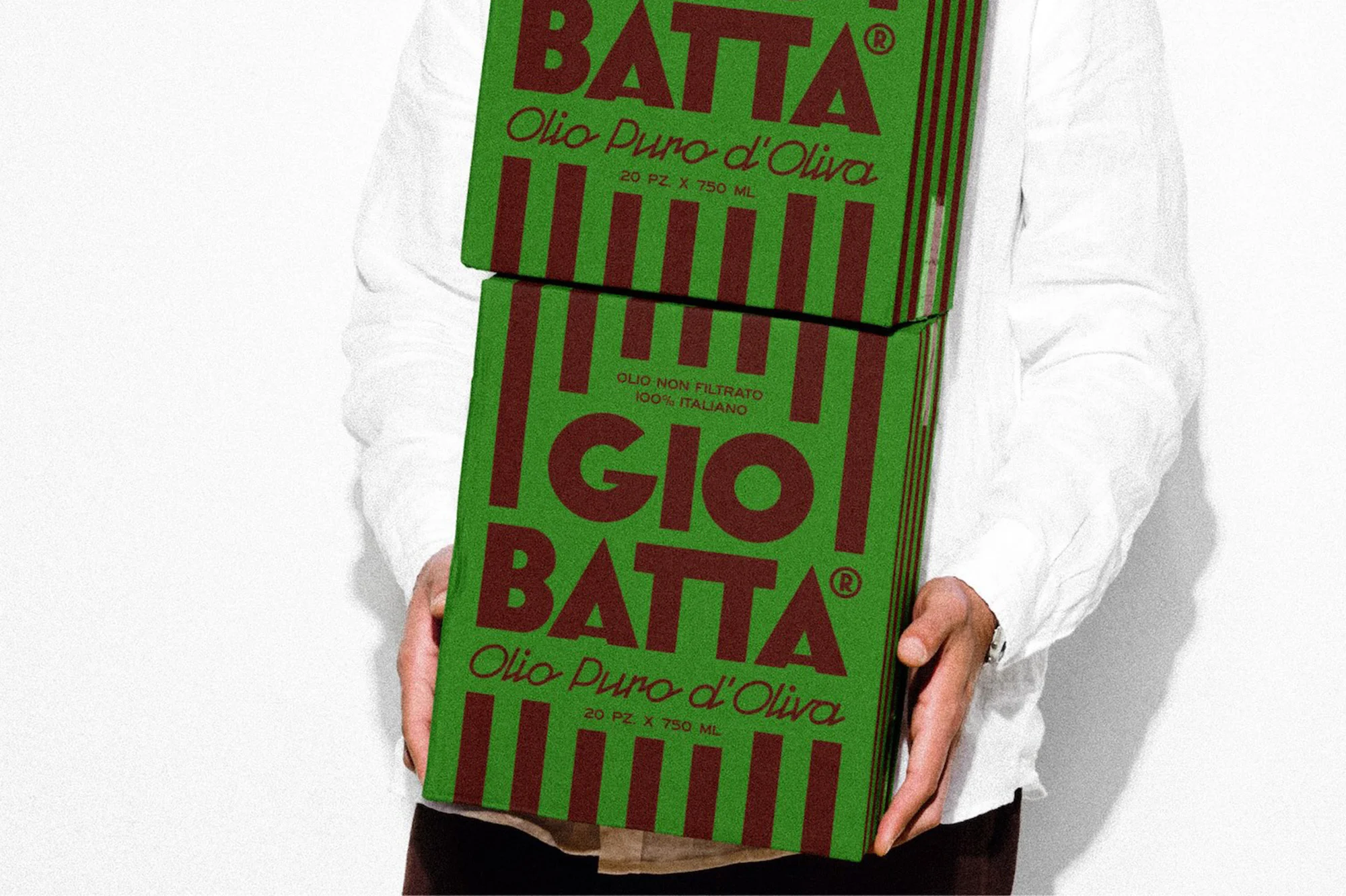 Person holds two Gio Batta olive oil boxes in a studio setting. The packaging is green with brown stripes and Italian text.