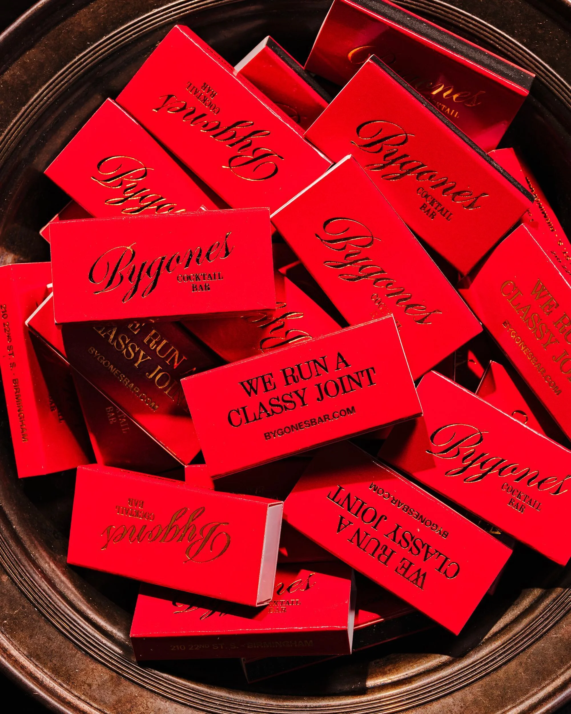 Close-up shot of Bygones cocktail bar matchbooks stacked in a silver bowl, featuring red packaging with gold lettering.