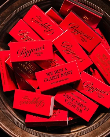 Close-up shot of Bygones cocktail bar matchbooks stacked in a silver bowl, featuring red packaging with gold lettering.